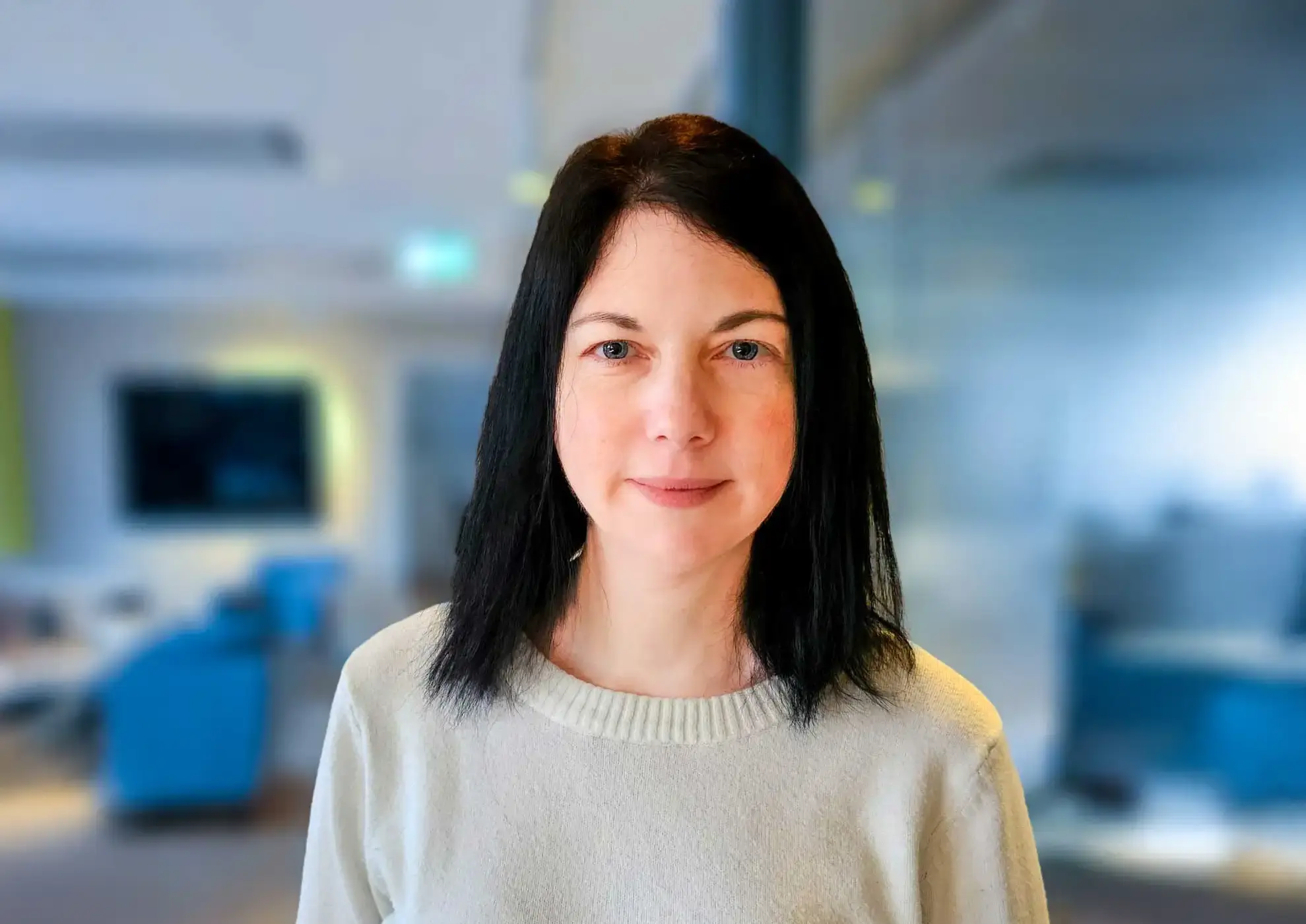 Foto på Therese Hagelin, anställd på E-identitet. Hon står i ett kontorslandskap och har mörkt hår som går ner till axlarna och bär en ljus tröja.